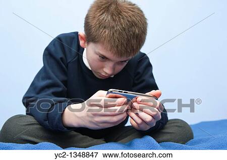 Stock Photo - A picture of an eleven year old boy playing with his ipod touch in his bedroom in the Uk. Fotosearch