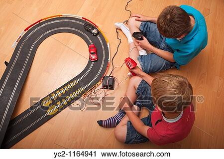 Stock Image - A picture of two boys 6 & 10 playing with a Hornby Scalextric racing car set game in the Uk. Fotosearch
