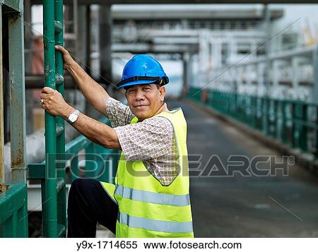 Stock Photography - A port worker climbs down a ladder after inspecting oil pipes at a shipping port in Johor, Malaysia. Fotosearch