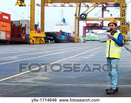 A port worker talking into a radio overseeing work at a commerical container and Palm Oil port in Johor, Malaysia View Large Photo Image Stock Photo - A port worker talking into a radio overseeing work at a commerical container and Palm Oil port in Johor, Malaysia. Fotosearch