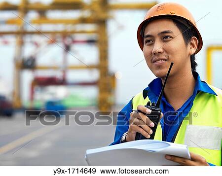 A port worker talking over and radio overseeing work at a commerical container and Palm Oil port in Johor, Malaysia View Large Photo Image Stock Photo - A port worker talking over and radio overseeing work at a commerical container and Palm Oil port in Johor, Malaysia. Fotosearch