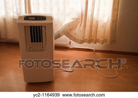 Stock Photo - A portable air conditioning unit in use indoors showing the outlet pipe going out of the window. Fotosearch