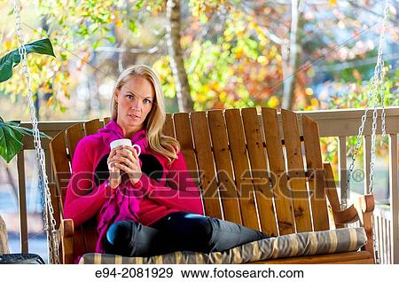 A portrait of a 39 year old blond woman wearing a sweater sitting on a porch swing holding a coffee cup, outdoors. View Large Photo Image Stock Photo - A portrait of a 39 year old blond woman wearing a sweater sitting on a porch swing holding a coffee cup, outdoors.. Fotosearch