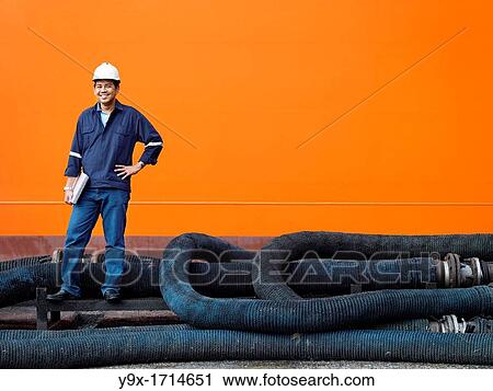 A portrait of a inspector at a commerical container and Palm Oil port in Johor, Malaysia standing on pipes by the hull of a ship View Large Photo Image Stock Image - A portrait of a inspector at a commerical container and Palm Oil port in Johor, Malaysia standing on pipes by the hull of a ship. Fotosearch