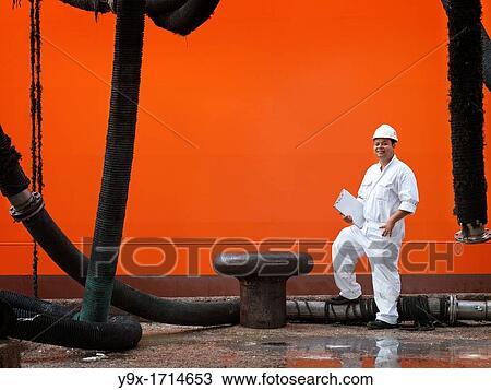 A portrait of a inspector at a commerical container and Palm Oil port in Johor, Malaysia standing on oil pipes by the hull of a ship View Large Photo Image Stock Image - A portrait of a inspector at a commerical container and Palm Oil port in Johor, Malaysia standing on oil pipes by the hull of a ship. Fotosearch
