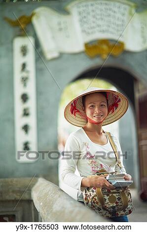 A portrait of a Vietnamese woman wearing a n? n lB or a traditional Vietnamese straw hat contrasted with modern clothes View Large Photo Image Stock Image - A portrait of a Vietnamese woman wearing a n? n lB or a traditional Vietnamese straw hat contrasted with modern clothes. Fotosearch