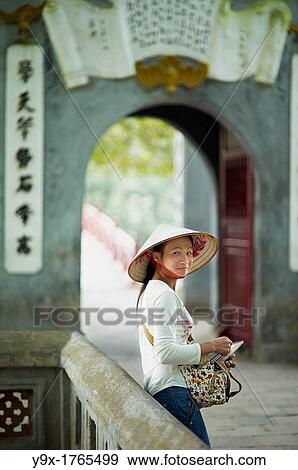 Stock Photo - A portrait of a Vietnamese woman wearing a n? n lB or a traditional Vietnamese straw hat contrasted with modern clothes. Fotosearch
