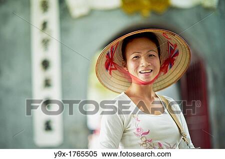 Stock Photography - A portrait of a Vietnamese woman wearing a n? n lB or a traditional Vietnamese straw hat contrasted with modern clothes. Fotosearch