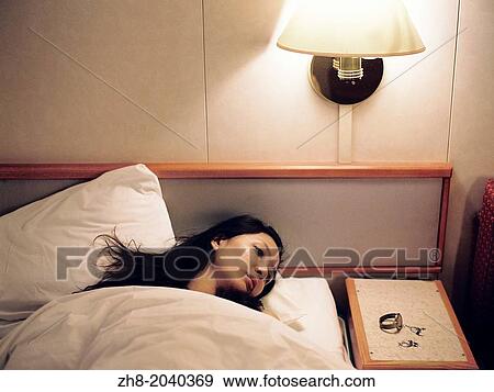 A portrait of a woman lying in a hotel bed with her watch and earrings on the bedside table. View Large Photo Image Stock Photo - A portrait of a woman lying in a hotel bed with her watch and earrings on the bedside table.. Fotosearch