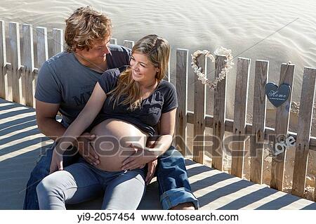 A pregnant woman and her partner sitting on the beach. View Large Photo Image Picture - A pregnant woman and her partner sitting on the beach.. Fotosearch