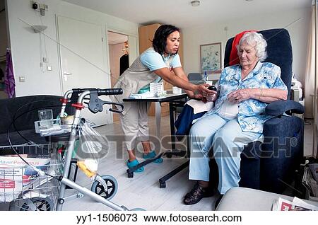 Stock Image - A professional nurse of a Rotterdam nursing home helping an elderly inhabitant with the controls of her chair.. Fotosearch