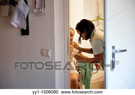 Stock Image - A professional nurse of a Rotterdam nursing home helping an elderly inhabitant getting dressed.. Fotosearch