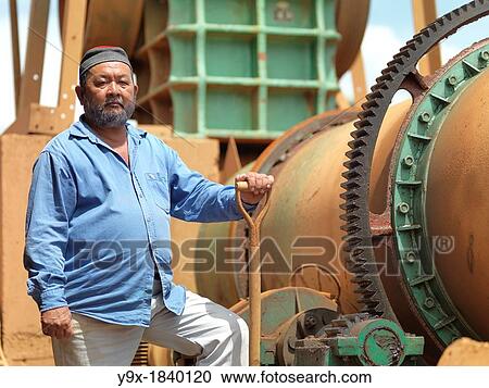Stock Image - A project manager on a tin mining operation in Johor, Malaysia standing proudly next to heavy machinery used in the extraction.. Fotosearch