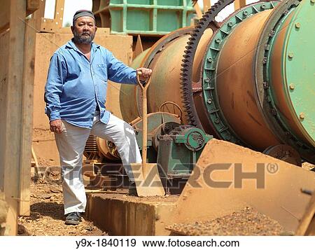Stock Photo - A project manager on a tin mining operation in Johor, Malaysia standing proudly next to heavy machinery used in the extraction.. Fotosearch