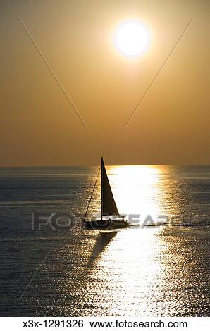 A sailboat navigating in the water with sunlight View Large Photo Image Stock Photograph - A sailboat navigating in the water with sunlight. Fotosearch