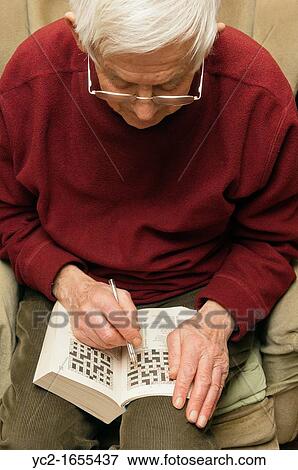 Stock Photo - A senior elderly man in his 80's doing a crossword puzzle at home in England, Britain, Uk. Fotosearch