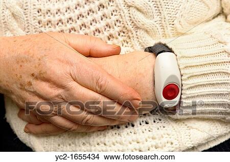 Picture - A senior elderly woman in her 70's with a home alarm unit on her wrist for emergencies at home in England, Britain, Uk. Fotosearch