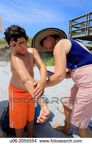 a senior woman applying sunscreen to her grandson at a beach View Large Photo Image Picture - a senior woman applying sunscreen to her grandson at a beach. Fotosearch