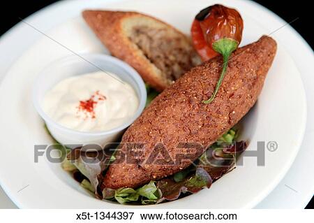 A serving of Kibbeh also kubbeh with Tehina and salad Kibbeh is meat and spices wrapped in bulgur and deep fried View Large Photo Image Stock Photo - A serving of Kibbeh also kubbeh with Tehina and salad Kibbeh is meat and spices wrapped in bulgur and deep fried. Fotosearch