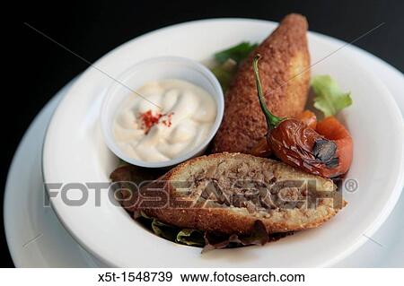 Stock Photo - A serving of Kibbeh also kubbeh with Tehina and salad Kibbeh is meat and spices wrapped in bulgur and deep fried. Fotosearch