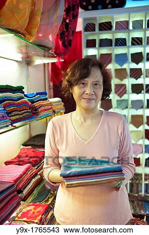 Stock Image - A shop owner shows off silk at the Nunal Boutique silk shop in Hanoi that sells colorful pieces of embroidered silk. Fotosearch