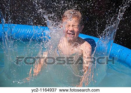 Stock Photo - A six year old boy splashing and showing movement in a small garden swimming pool in the Uk. Fotosearch