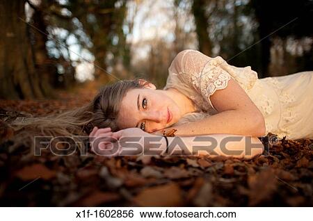 Stock Photograph - a slim blonde woman girl alone in woodland autumn afternoon daytime UK. Fotosearch
