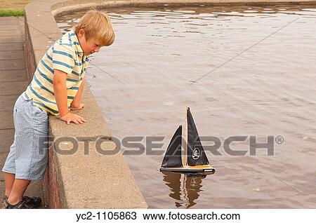 A small boy sailing his toy boat at the boating lake in Aldeburgh, Suffolk, Uk View Large Photo Image Stock Image - A small boy sailing his toy boat at the boating lake in Aldeburgh, Suffolk, Uk. Fotosearch