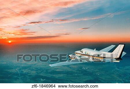 Picture - A small twin engine commuter plane flies into the beautiful orange sunset. Fotosearch
