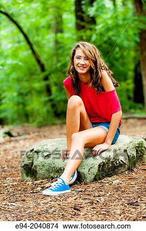 A smiling 14 year old brunette girl in shorts, sneakers and a red top in a forest setting. View Large Photo Image Picture - A smiling 14 year old brunette girl in shorts, sneakers and a red top in a forest setting.. Fotosearch