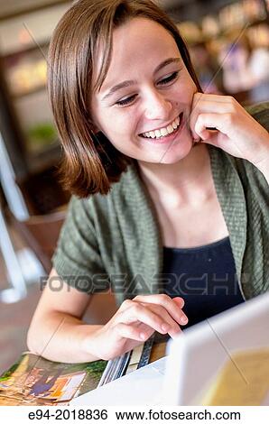 A smiling 18 year old girl in a library reading from a computer screen. View Large Photo Image Stock Photograph - A smiling 18 year old girl in a library reading from a computer screen.. Fotosearch