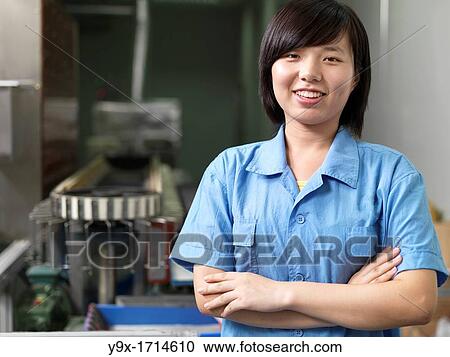 Stock Image - A smiling factoy worker standing near industrial equipment in a Li-ion Battery Co which develops, manufactures, and markets cylindrical type rechargeable Li-ion batteries. Fotosearch