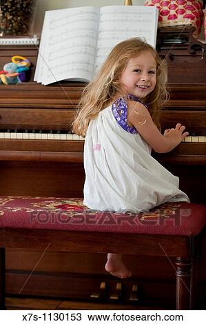 Stock Image - A smiling young girl sitting at the piano. Fotosearch
