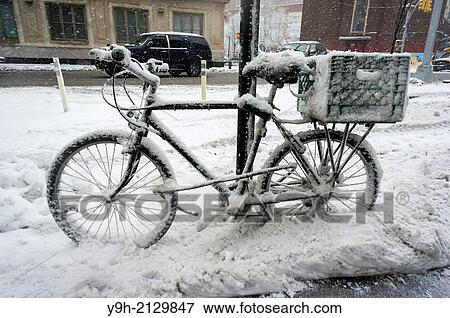 Stock Photo - A snow encrusted bicycle chained to a pole in the Chelsea neighborhood of New York. A winter storm with wet, slushy snow is hitting the city with an expected snowfall of 4 to 8 inches.. Fotosearch