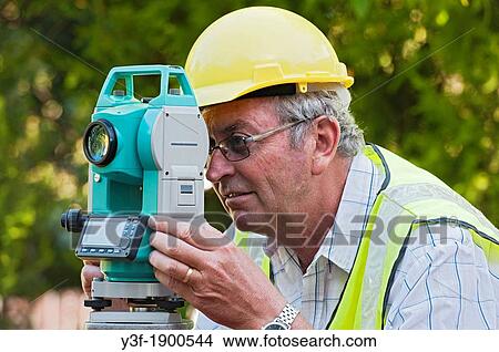 Picture - A surveyor on a building site takes measurements using his theodolite. Fotosearch