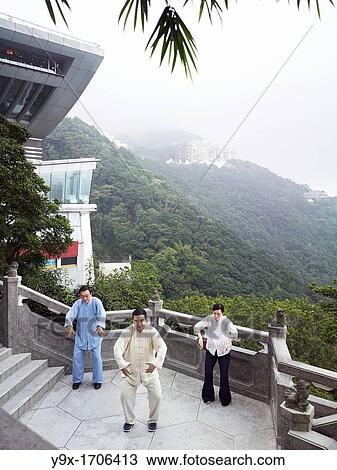 Stock Image - A Tai Chi Master and his student practice martial arts at The Peak with The Peak Tower in background. Fotosearch