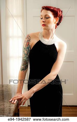 A tattooed 24 year old red headed woman wearing a small black dress indoors. View Large Photo Image Stock Photo - A tattooed 24 year old red headed woman wearing a small black dress indoors.. Fotosearch