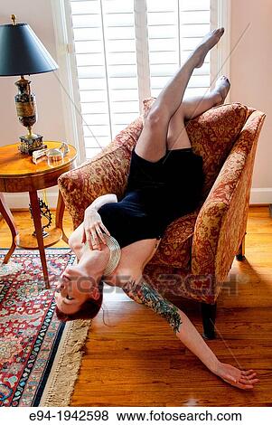 A tattooed 24 year old red headed woman wearing a small black dress indoors reclining upside down in a chair. View Large Photo Image Stock Photo - A tattooed 24 year old red headed woman wearing a small black dress indoors reclining upside down in a chair.. Fotosearch