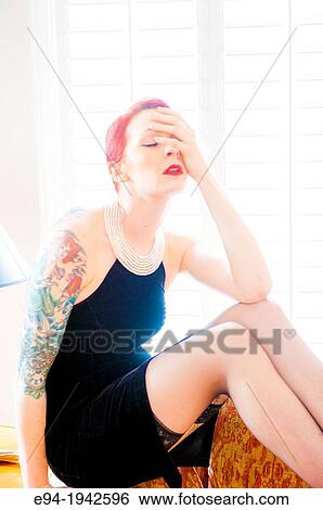 A tattooed 24 year old red headed woman wearing a small black dress indoors with her hand covering part of her face. View Large Photo Image Stock Photograph - A tattooed 24 year old red headed woman wearing a small black dress indoors with her hand covering part of her face.. Fotosearch