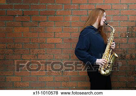 A teenage girl playing saxaphone, leaning against a brick wall View Large Photo Image Stock Photo - A teenage girl playing saxaphone, leaning against a brick wall. Fotosearch