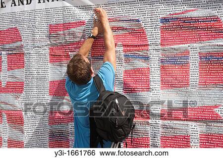 Stock Photograph - A visitor marks a name on the list of those who perished in the 9/11 terrorist attack of the World Trade Center. The list is posted on Greenwich Street across from the entrance to the National September 11 Memorial in New York City, New York, USA. Fotosearch