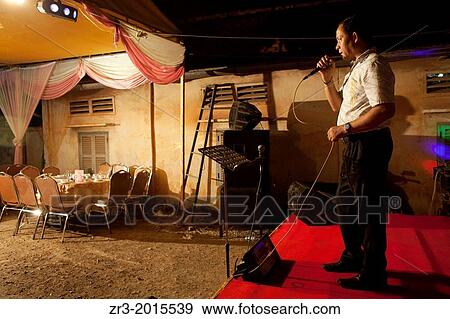 A wedding guest sings karaoke to empty seats at buddhist wedding in a small village outside of Phnom Penh, Cambodia. View Large Photo Image Stock Photo - A wedding guest sings karaoke to empty seats at buddhist wedding in a small village outside of Phnom Penh, Cambodia.. Fotosearch