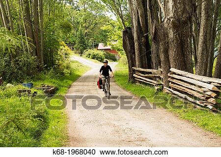 Stock Image - A woman, 66, bicycles on a country road on Saturna Island, Gulf Islands, British Columbia, Canada. Fotosearch