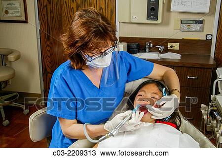 A woman dentist cleans her Asian American girl patient's teeth in Newport Beach, CA. Note surgical mask and latex gloves. MODEL RELEASE. View Large Photo Image Stock Image - A woman dentist cleans her Asian American girl patient's teeth in Newport Beach, CA. Note surgical mask and latex gloves. MODEL RELEASE.. Fotosearch