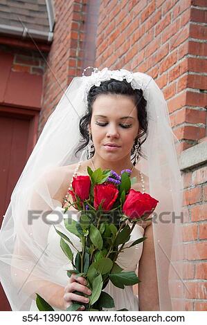 Stock Photograph - A woman in a bridal gown and holding red roses by a church in Rosalia, Washington, USA.. Fotosearch