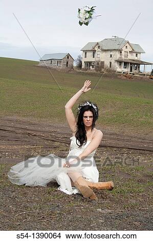Picture - A woman in a bridal gown, crying and sitting in a desolate field, throwing her flowers up in the air.. Fotosearch