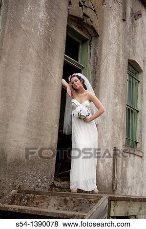 Stock Photo - A woman in a bridal gown, standing by an old building. Fotosearch