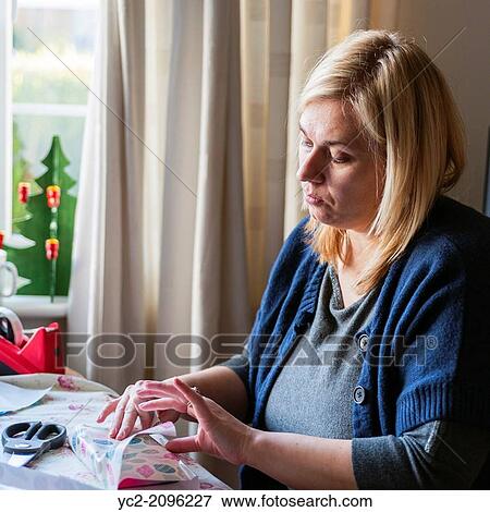 Stock Photo - A woman in her 30's wrapping Christmas presents up at home in the Uk.. Fotosearch