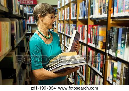 A woman librarian holds books beside bookshelf in library. View Large Photo Image Picture - A woman librarian holds books beside bookshelf in library.. Fotosearch
