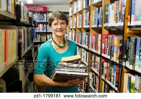 A woman librarian holds books beside bookshelf in library View Large Photo Image Stock Image - A woman librarian holds books beside bookshelf in library. Fotosearch